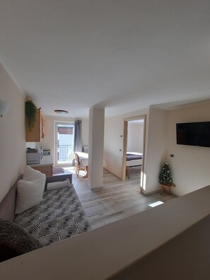 A modern apartment with a living room, dining area, kitchenette, and a small balcony.
