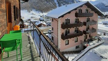 A wooden building with a balcony, a pink building in the background, and snow-covered mountains.