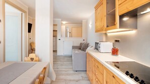 A compact kitchen with wooden cabinets, a microwave, a toaster, and a stove. - Apartment 'Appartamento Zefiro' with Mountain View, Balcony and Wi-Fi (Livigno)