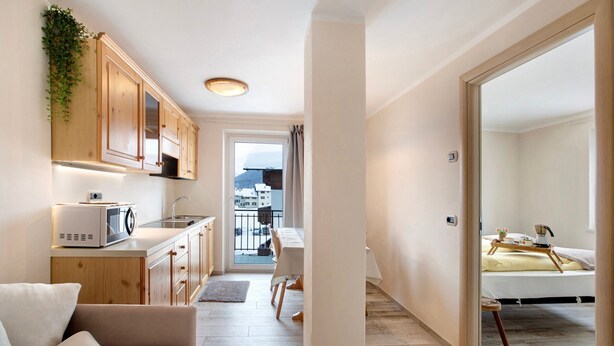 A compact living space with a kitchenette, a dining area, and a bedroom with a bed and bedside table. - Apartment 'Appartamento Zefiro' with Mountain View, Balcony and Wi-Fi (Livigno)