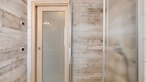 A bathroom with a wooden wall, a frosted glass door, and a shower area. - Apartment 'Appartamento Zefiro' with Mountain View, Balcony and Wi-Fi (Livigno)