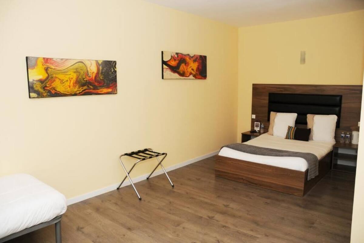 A bedroom with a wooden bed, two paintings on the wall, a nightstand, and a small folding chair.
