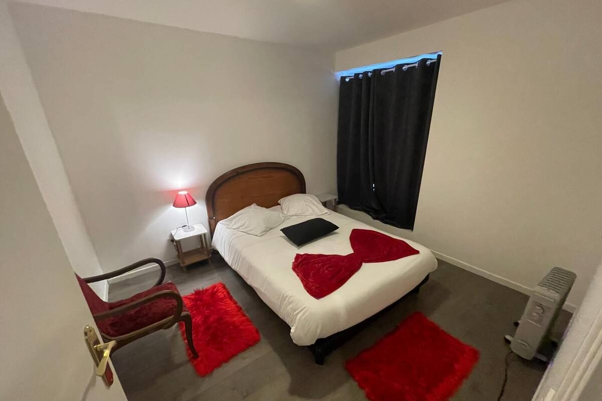 A hotel room with a bed, a nightstand, a lamp, a chair, and a heater.