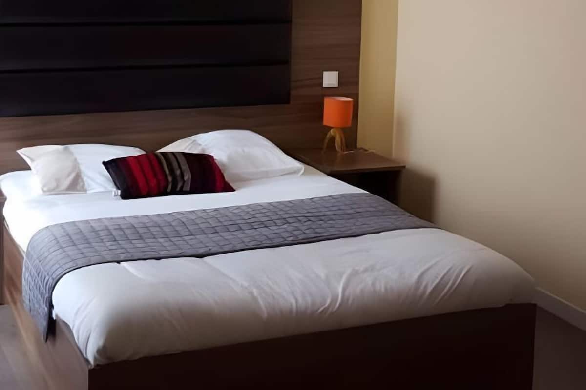 A neatly made bed with a dark headboard, white bedding, and a grey quilted throw.