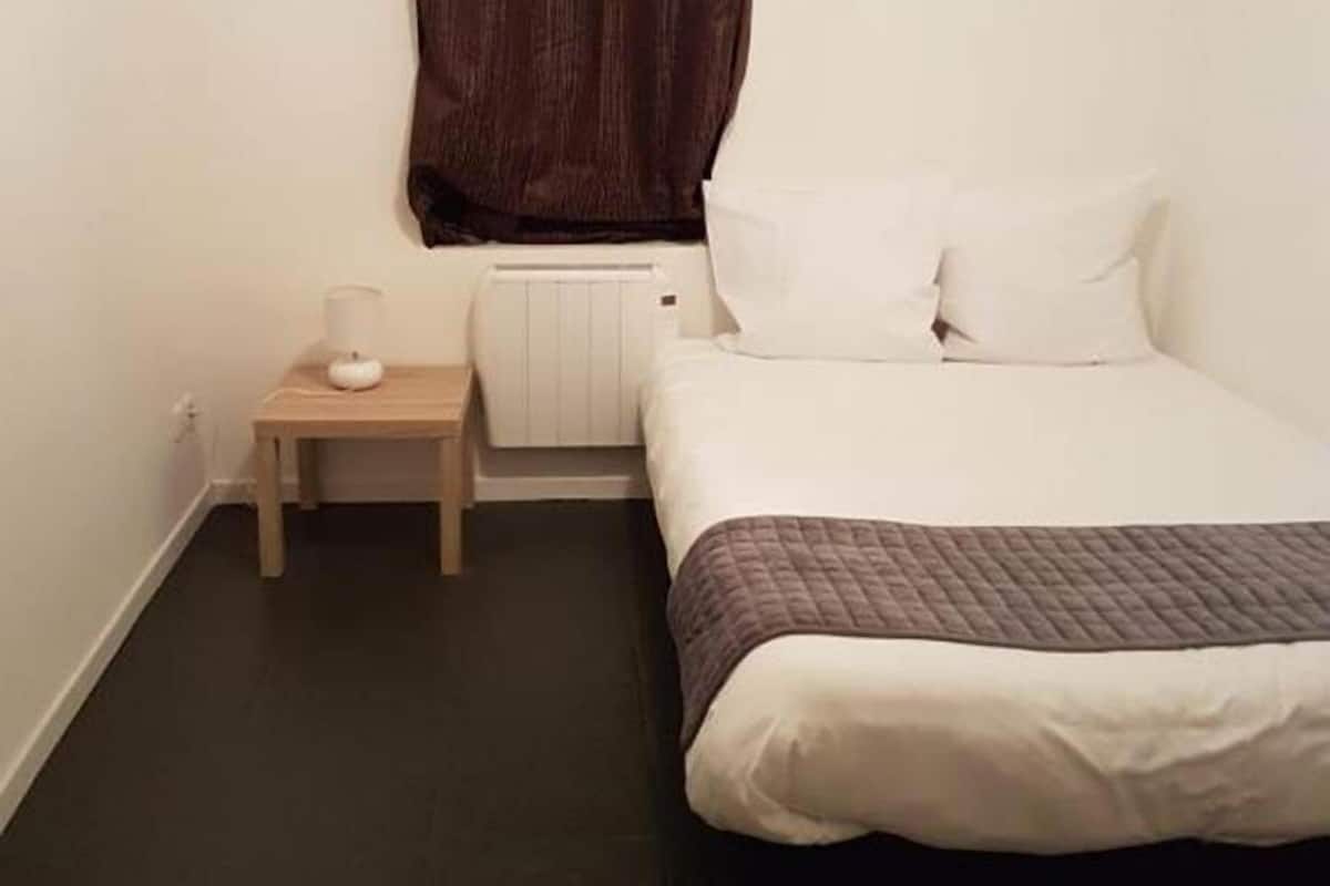 A small, neatly arranged bedroom with a single bed, a bedside table with a lamp, and a radiator.
