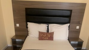 Una cama grande con cabecera de madera, dos mesitas de noche y una única almohada decorativa.