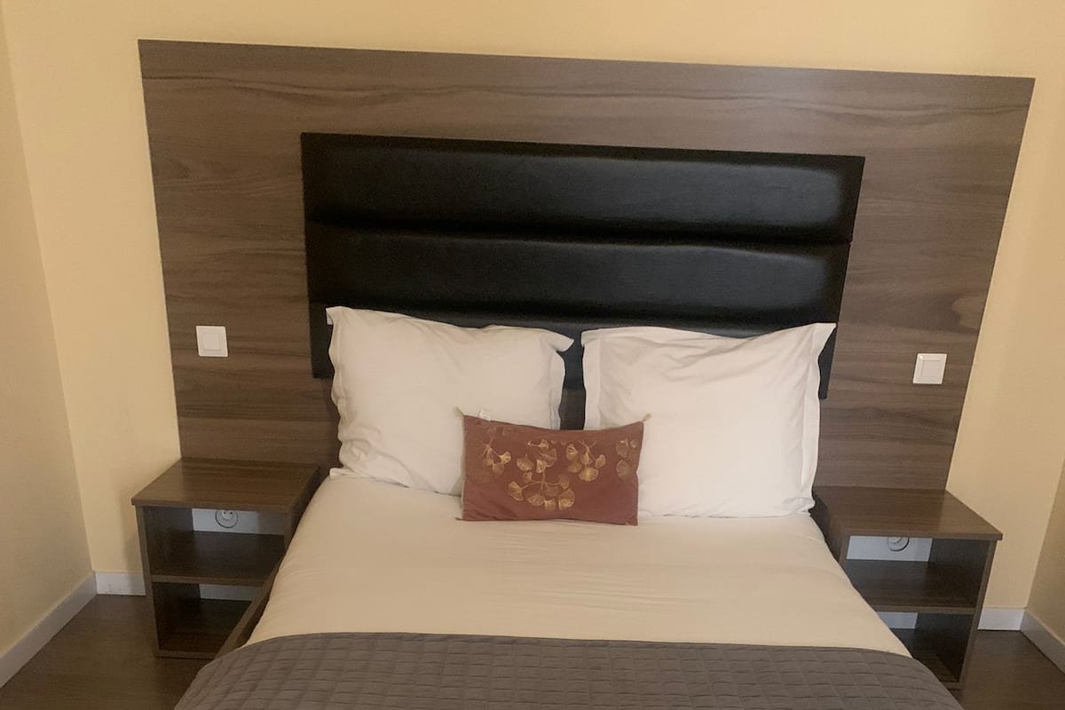 A large bed with a wooden headboard, two bedside tables, and a single decorative pillow.