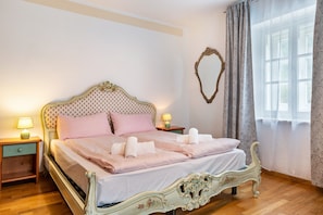 Un lit avec une tête de lit décorative, deux tables de chevet avec des lampes, un miroir au mur et une fenêtre avec des rideaux.