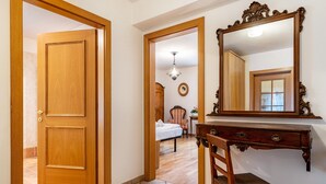 Eine Holztür, ein Spiegel, ein Stuhl, ein Bett und eine Kommode in einem Raum mit Fliesenboden.