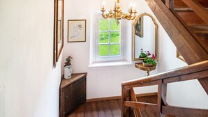 Eine Holztreppe, ein Fenster mit Blick auf Grünflächen und ein Spiegel an der Wand.