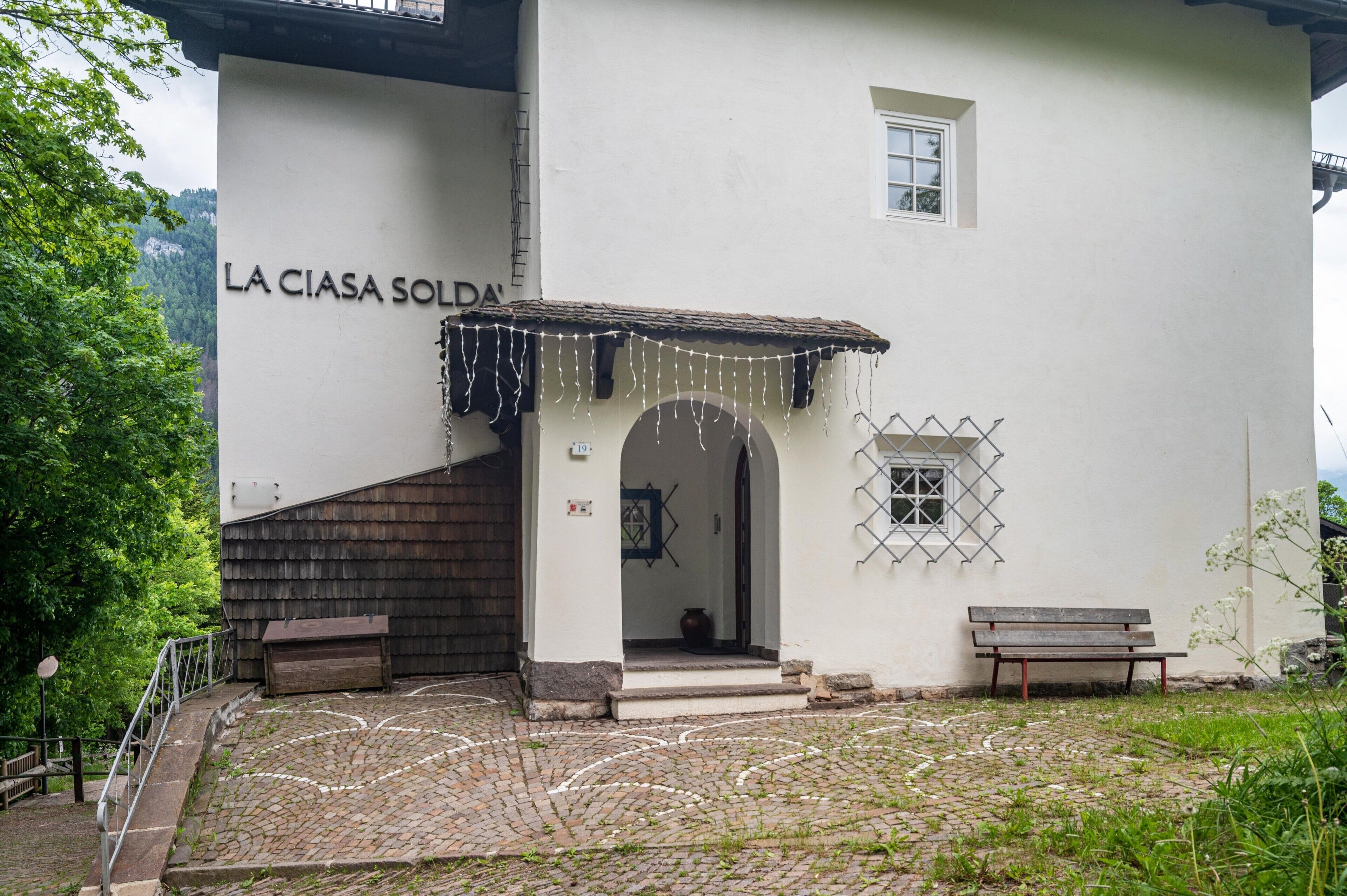 Ein Gebäude mit weißer Fassade, einer Holzbank, einem Kopfsteinpflasterhof und einem Schild mit der Aufschrift 'LA CIASA SOLDA'.