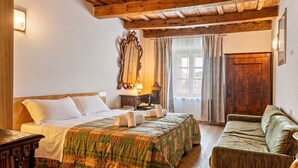 Ein Zimmer mit Holzboden, einem Bett mit grün-orangefarbener Bettdecke, einem Nachttisch aus Holz, einem grünen Sofa und einer Holztür.