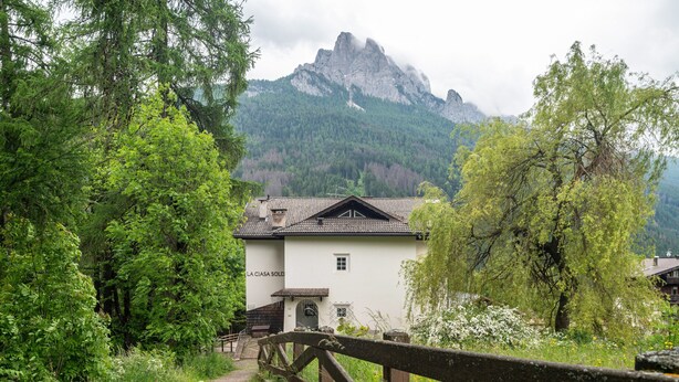 Ein weißes Gebäude mit einem Ziegeldach, umgeben von üppiger Vegetation und einem Holzzaun.