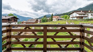 Holzgeländer eines Balkons mit Blick auf eine gebirgige Landschaft und traditionelle Gebäude.