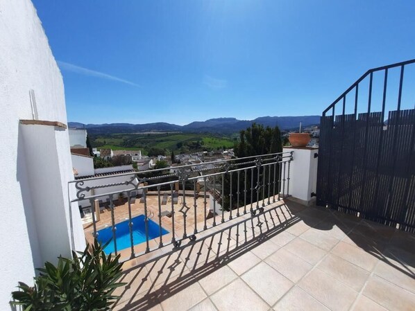 A balcony with a view of a pool and distant hills.