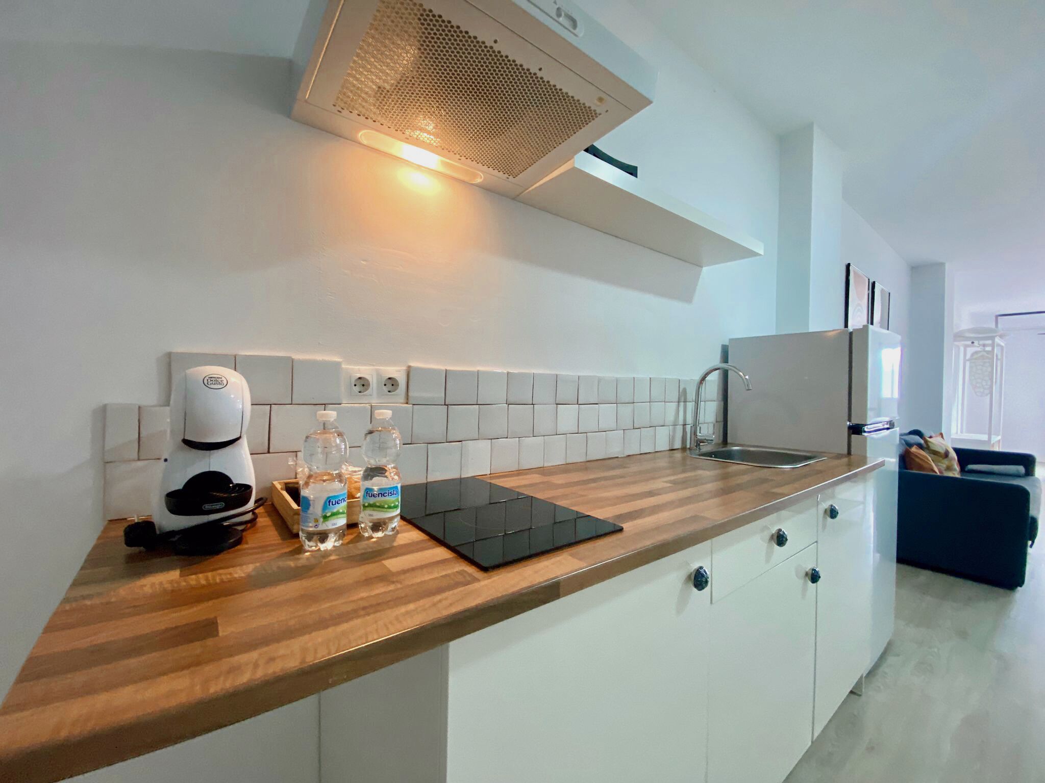 Una cocina moderna con encimera de madera, cafetera, botellas de agua y una tableta negra.