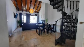 Amplia sala de estar con techo de madera, una escalera espiral negra y un comedor con mesa y sillas.