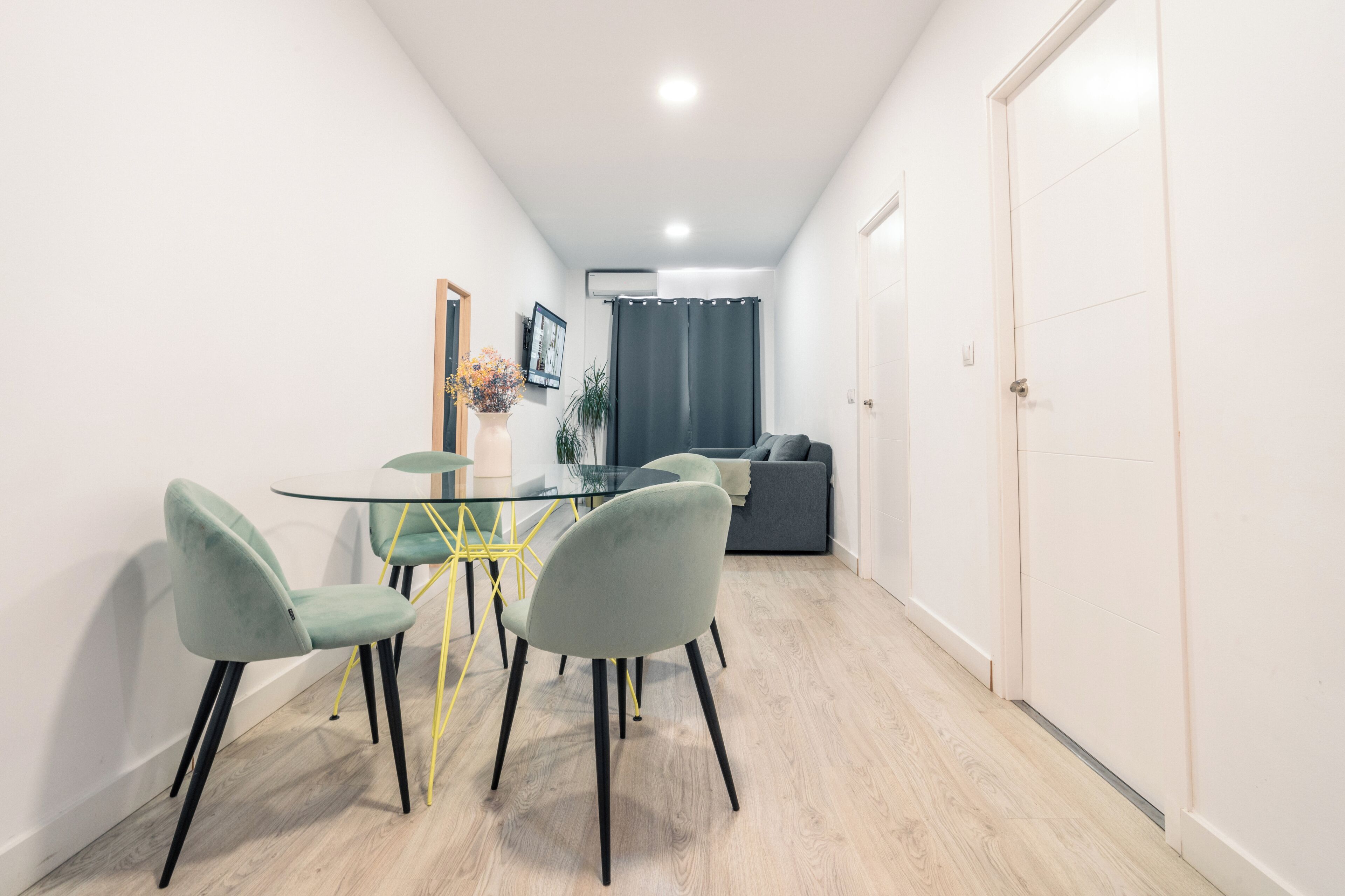 A modern dining area with a glass table, four chairs, and a yellow metal frame.