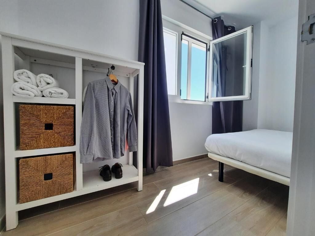 A bedroom with a bed, a wardrobe with folded clothes, and a window with curtains.