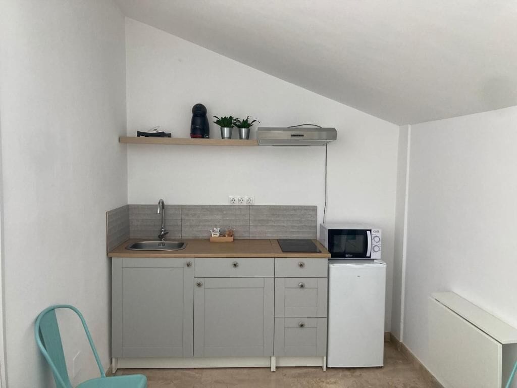 A compact kitchen with a sink, microwave, and small refrigerator. There is a wooden countertop and a shelf above the sink.