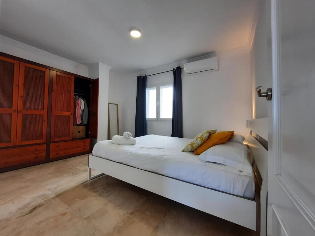 A bedroom with a bed, a wardrobe, a window with curtains, and an air conditioning unit.