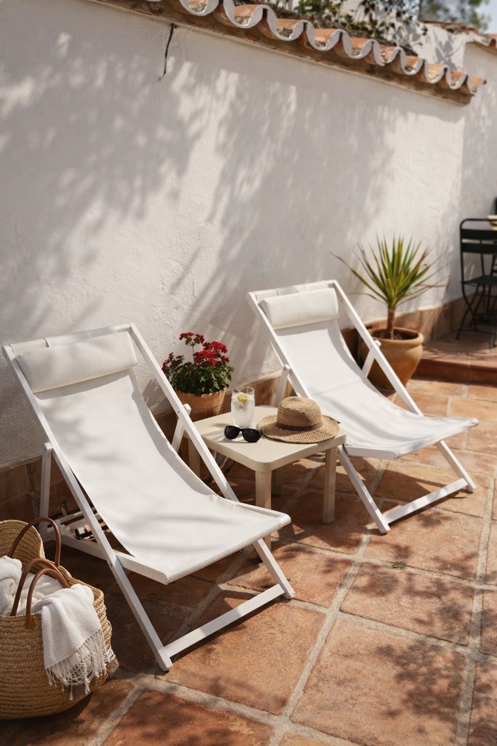 Deux fauteuils de jardin blancs, une petite table sur laquelle est posée une plante en pot et un panier en osier contenant une serviette.