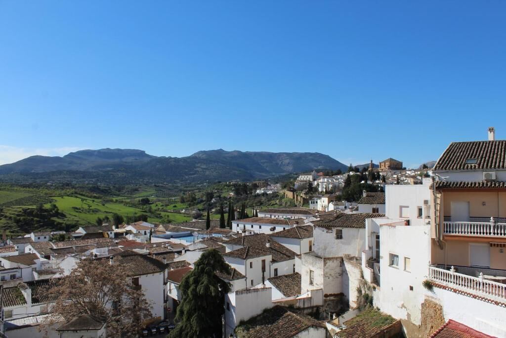 A town with white buildings and red-tiled roofs, surrounded by green hills and mountains.