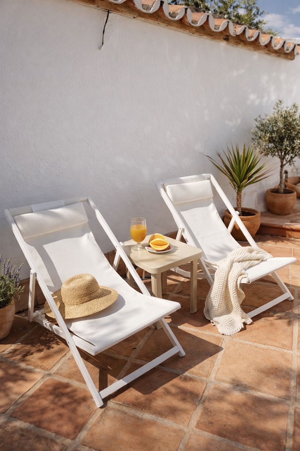 Zwei weiße Lounge-Stühle mit Kissen, ein kleiner Tisch mit Orangensaft und einer Speiseplatte, sowie Topfpflanzen.