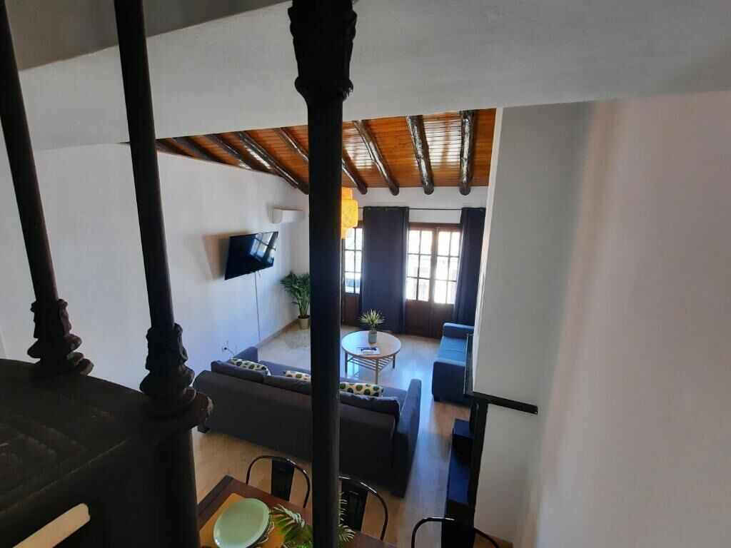 A spacious living area with a high ceiling, a flat-screen TV mounted on the wall, and a dining table with chairs.