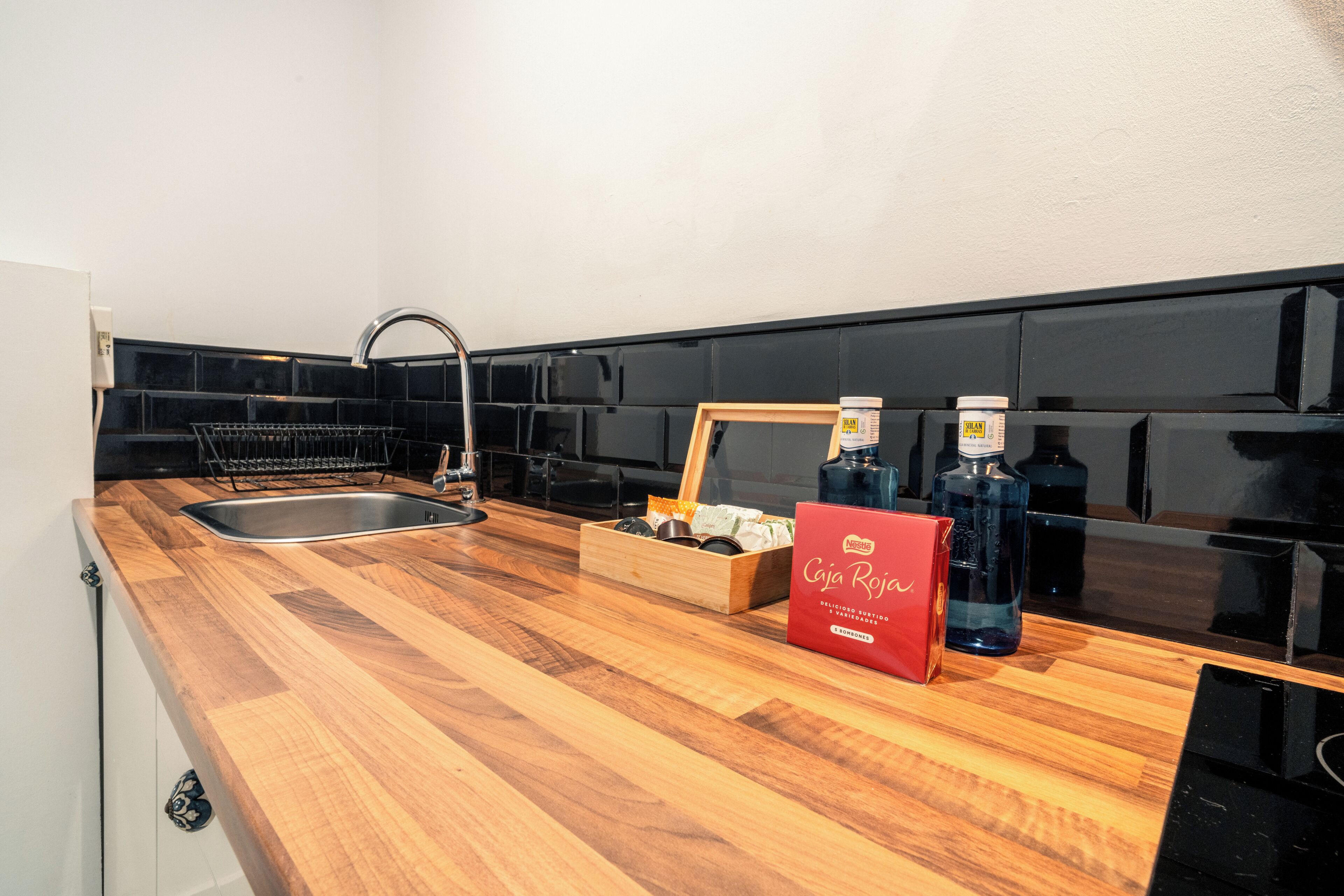 A kitchen with a wooden countertop, a stainless steel sink, black tiled backsplash, and a red box labeled 'Cajita Roja'.