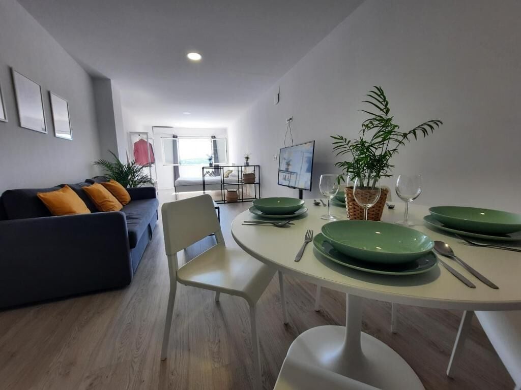 A modern living room with a sofa, a dining table set with green plates, and a potted plant.