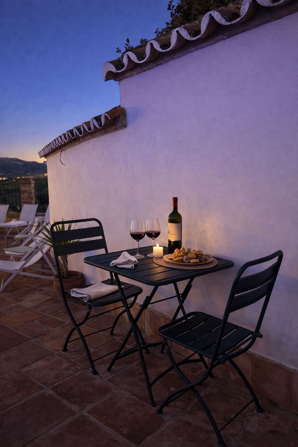Un patio con una mesa dispuesta para dos personas, una botella de vino y una vela.