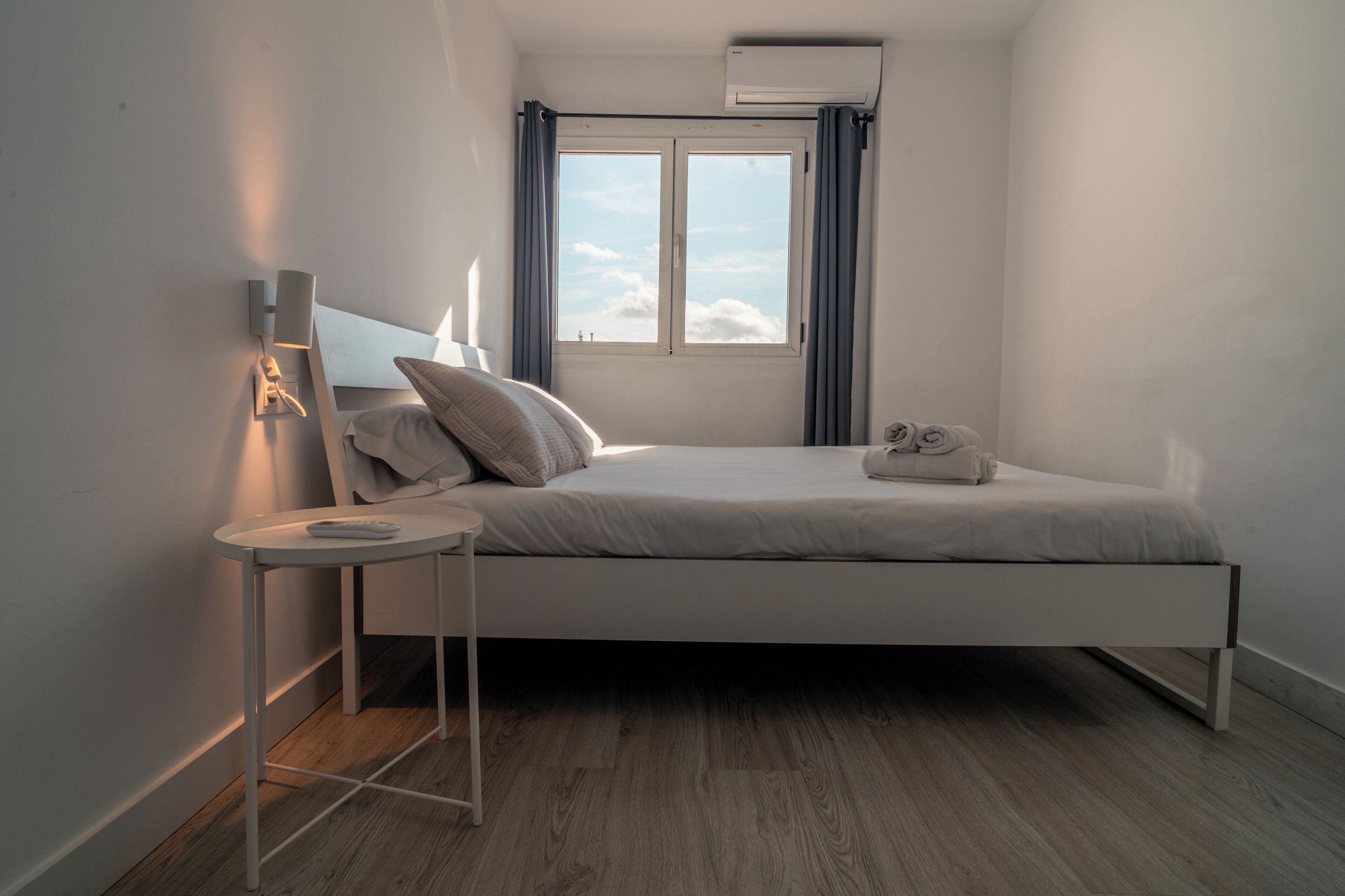 A modern bedroom with a bed, bedside table, lamp, and window with curtains.