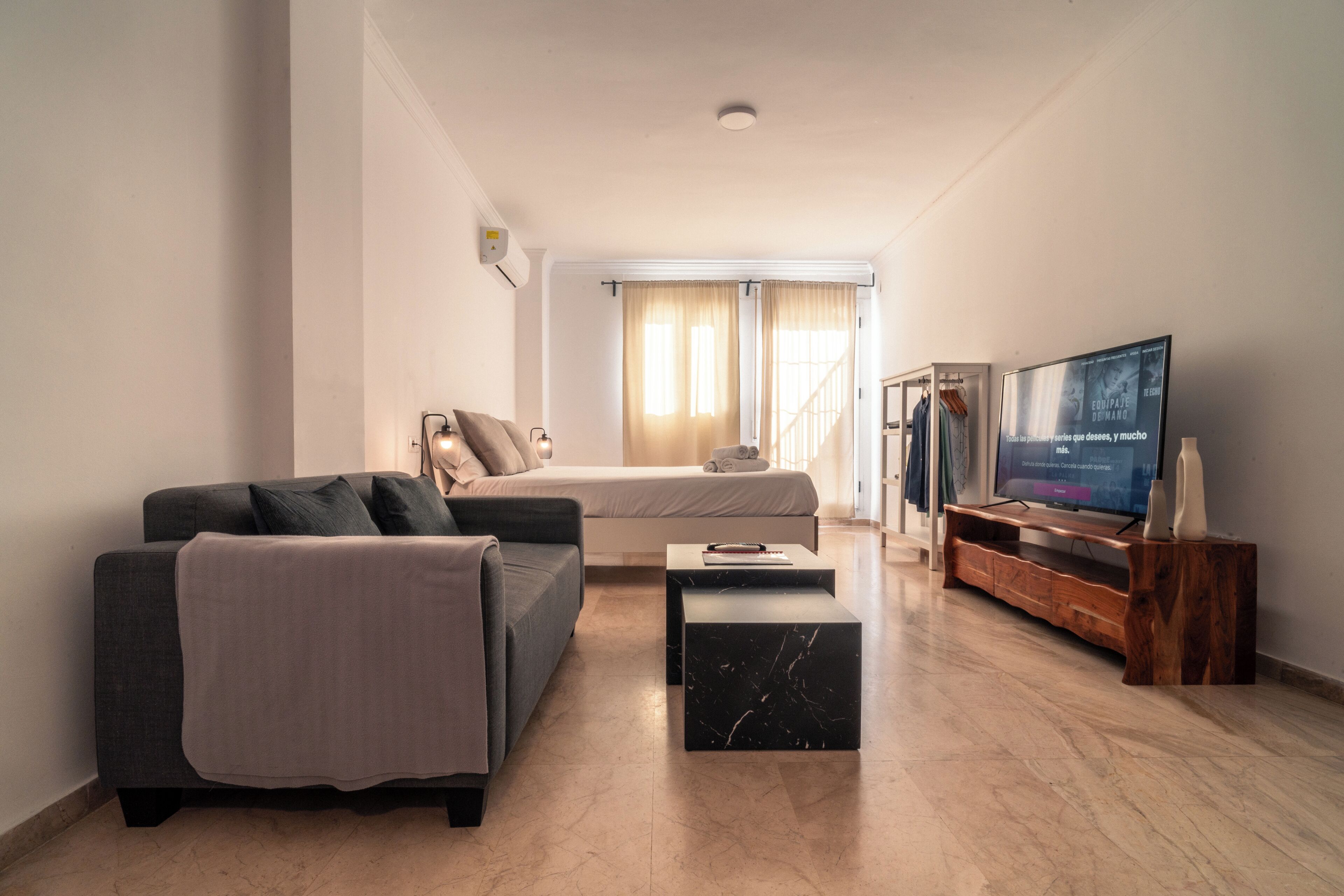 Un soggiorno moderno con un divano, un letto, una TV e un mobile TV in legno.