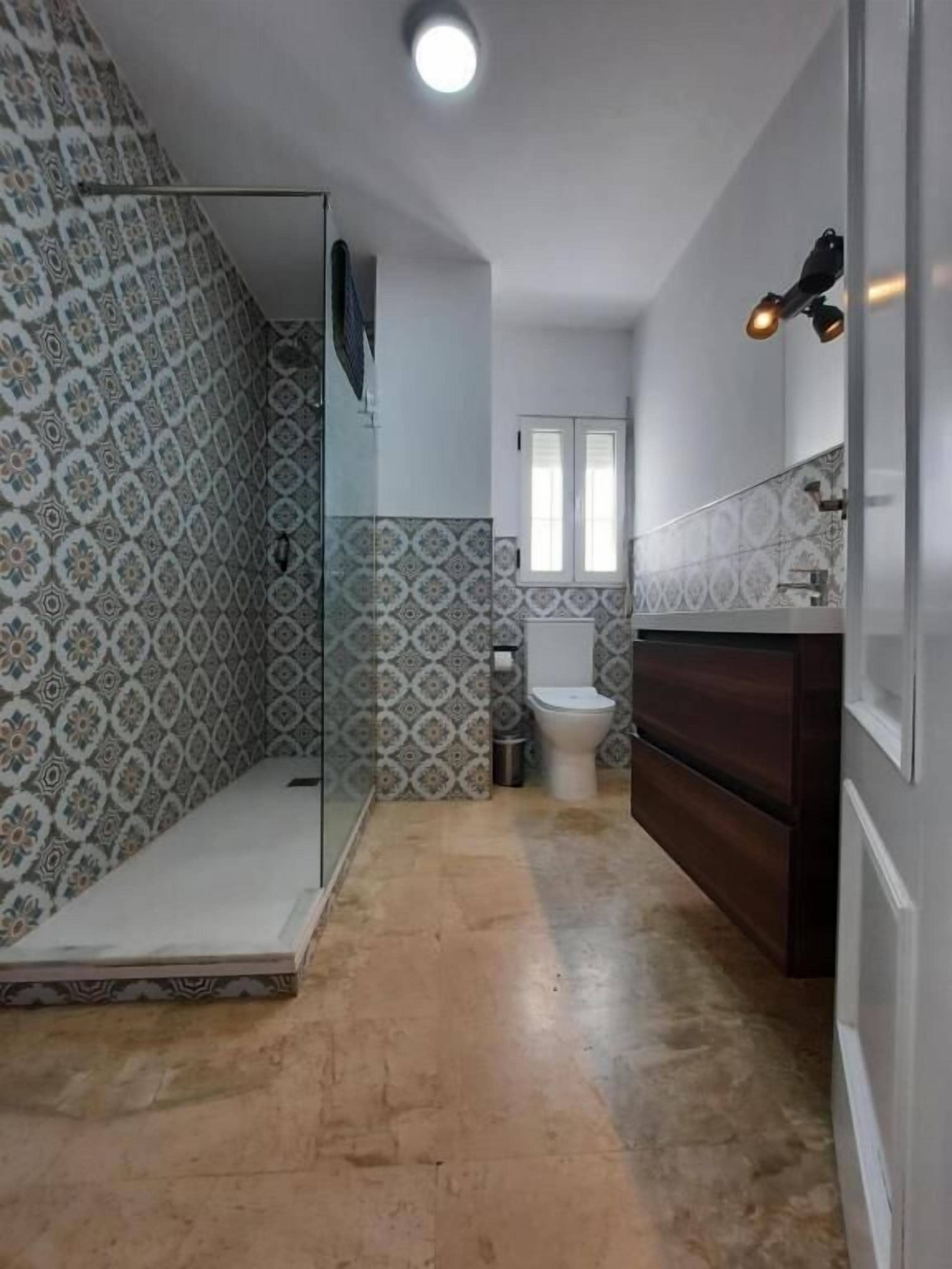 A bathroom with patterned tiles, a glass shower enclosure, a toilet, and a dark wooden vanity.