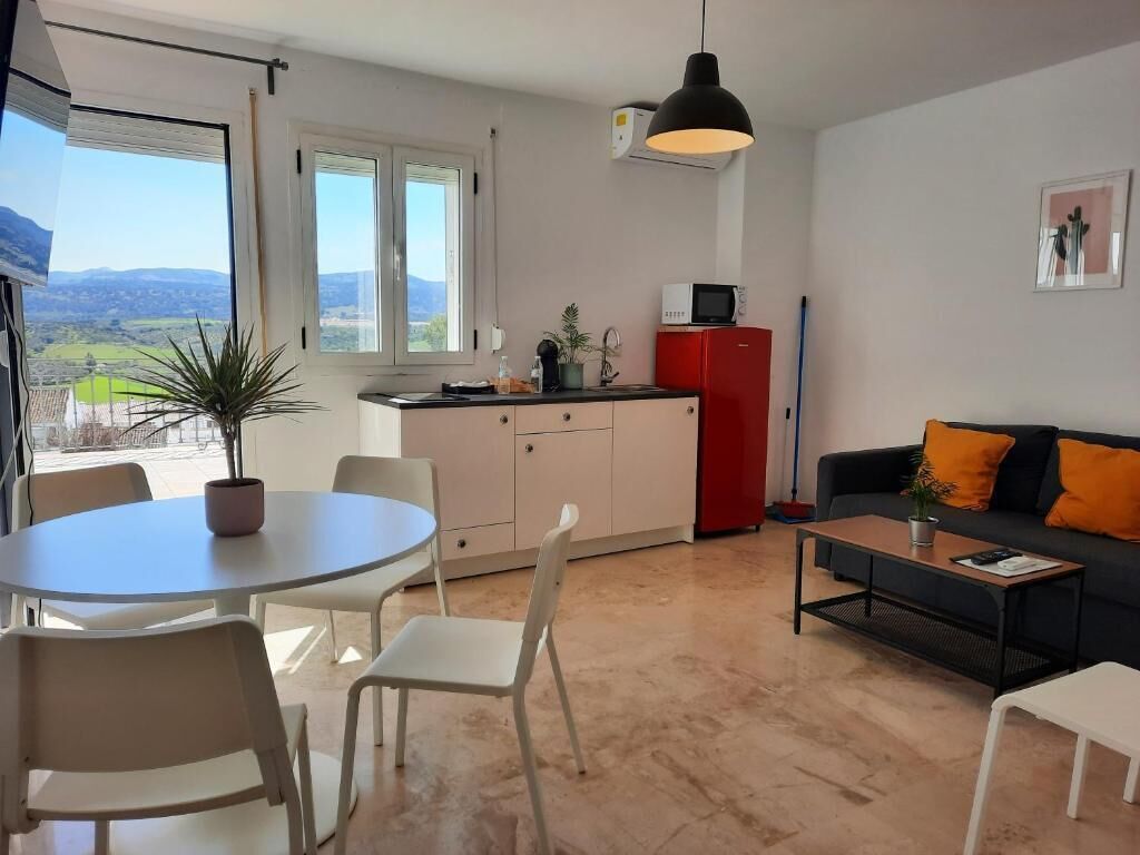 A modern living room with a dining area, a red refrigerator, and a view of the outdoors.