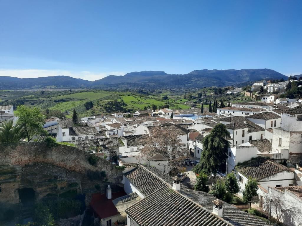 Une ville aux bâtiments blancs et aux toits en tuiles rouges, entourée de collines verdoyantes et de montagnes.