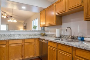 A kitchen with wooden cabinets, granite countertops, a stainless steel sink, and a ceiling fan. - Cozy House w/ Pool, Near State Farm Stadium (Glendale)