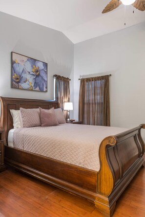 A bedroom with a large bed, wooden headboard, a nightstand, a lamp, and a ceiling fan. - Cozy House w/ Pool, Near State Farm Stadium (Glendale)