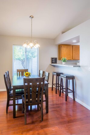 A dining area with a wooden table and chairs, a hanging light fixture, and a window with blinds. - Cozy House w/ Pool, Near State Farm Stadium (Glendale)