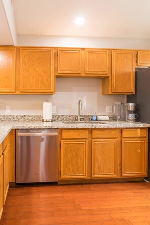 A kitchen with wooden cabinets, a stainless steel dishwasher, a coffee maker, and a sink. - Cozy House w/ Pool, Near State Farm Stadium (Glendale)