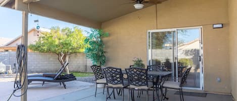 Un patio techado con una mesa y sillas, un ventilador de techo y un ventanal corredizo.