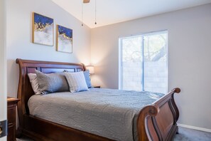 A bedroom with a wooden bed, a nightstand, a lamp, and two framed artworks on the wall. - Cozy House w/ Pool, Near State Farm Stadium (Glendale)