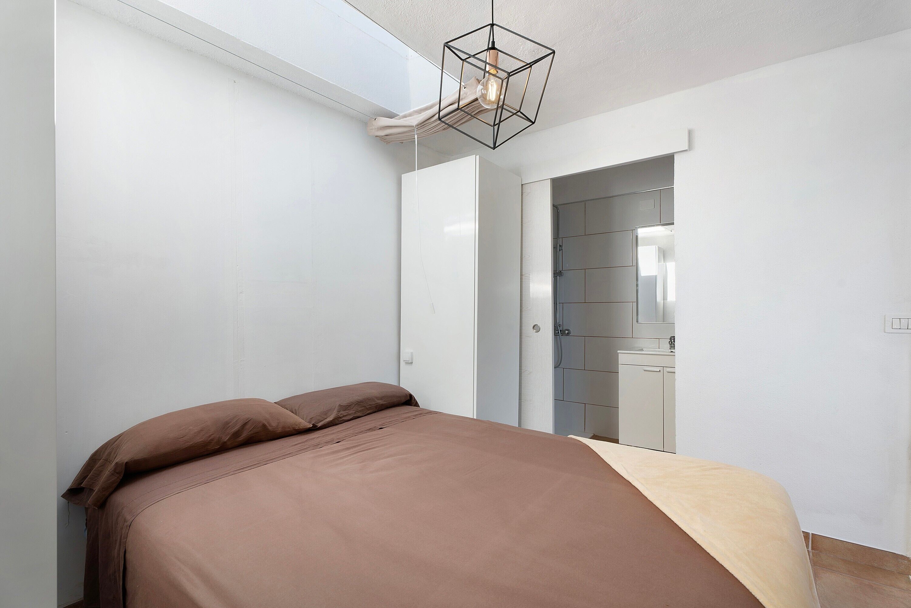 A bedroom with a bed, a skylight, and a view into a bathroom.