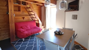 A cozy room with a wooden interior, a red sofa, a dining table with chairs, and a staircase leading to an upper level.