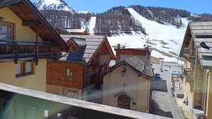 A row of wooden buildings with a church in the center, set against a backdrop of snow-covered mountains.
