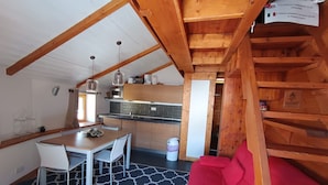 A cozy kitchen with a dining area, wooden beams, and a red sofa.