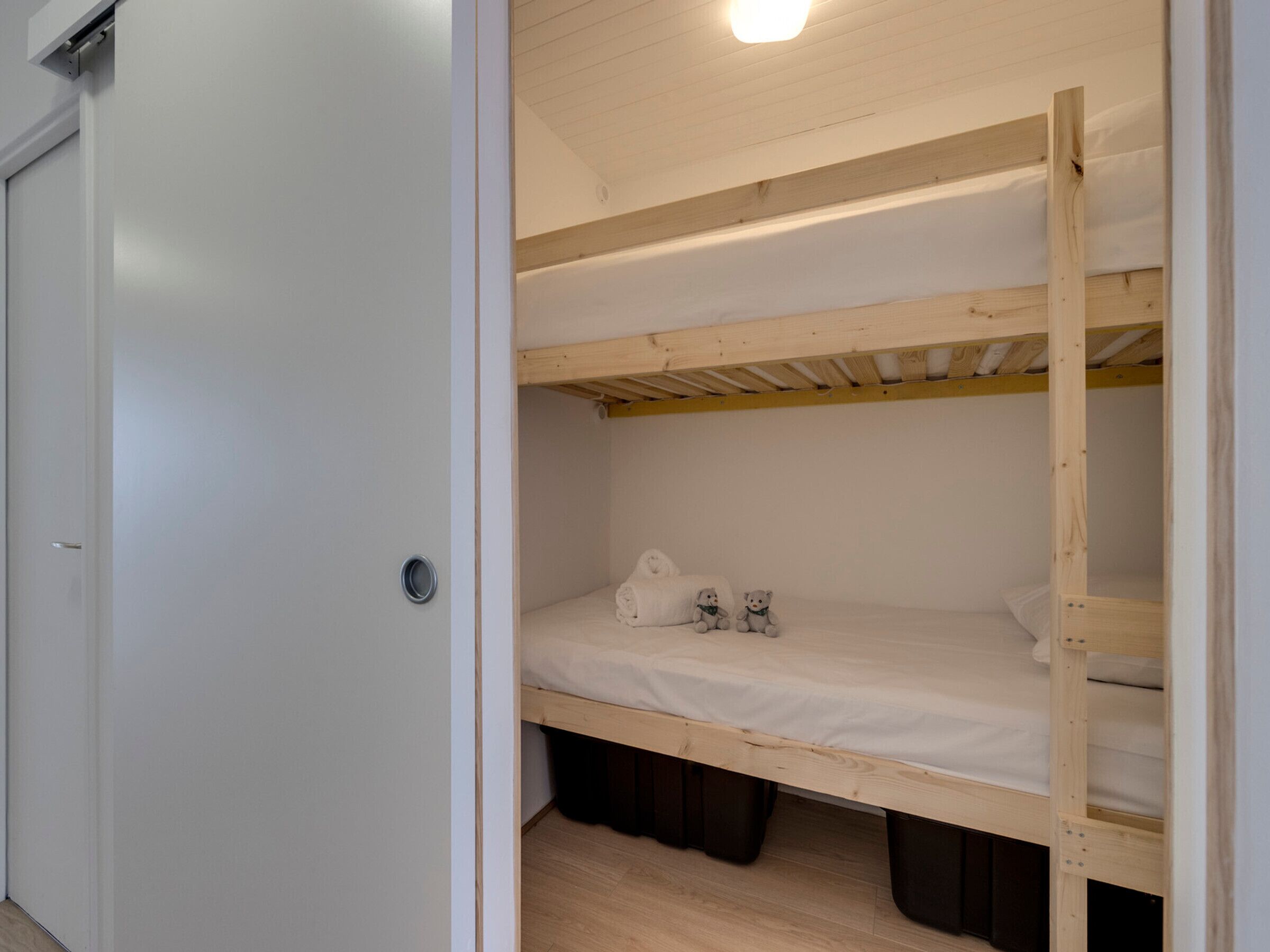 A bunk bed with two levels, a white door, and a light fixture above the bed.