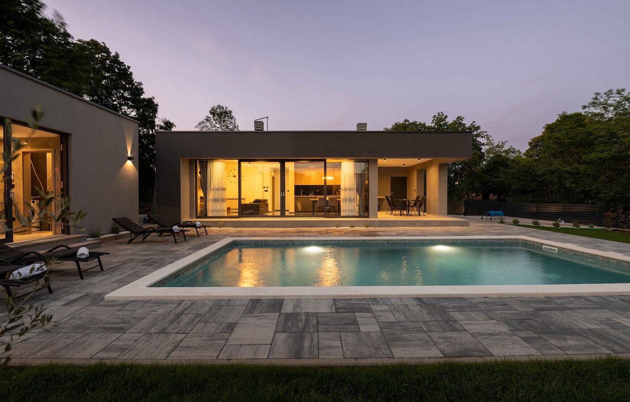 Ett modernt hus med en swimmingpool, utomhusmöbler och en väl upplyst interiör.