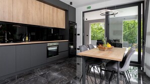 A modern kitchen with a wooden upper cabinet, a built-in oven, and a dining area with a table and chairs. - Amazing home in Nedescina with sauna (Nedescina)